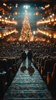 Couple walking down steps in a theater filled with audience and a large decorated Christmas tree in the background photo