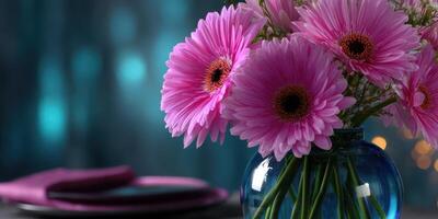 Vibrant pink gerbera daisies in a glass vase on a dining table with soft blue background photo
