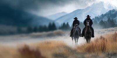 Cowboys ride horses through misty landscape with mountains in the background during early morning photo