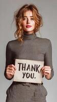 Woman expresses gratitude holding a thank you sign in a studio setting while dressed in a textured outfit photo