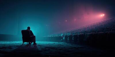 Man sits alone in an empty theater illuminated by vibrant blue and pink lights during a quiet evening photo