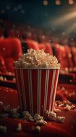 Popcorn overflowing from a striped bucket in a nearly empty movie theater at night photo