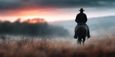 Cowboy riding a horse at sunset in a misty landscape with distant hills photo