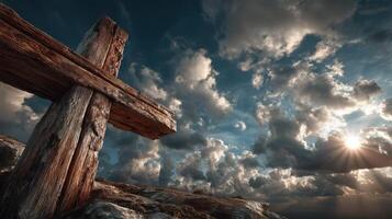 Wooden cross stands against a dramatic sky filled with clouds and sunlight at dusk photo