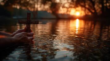 Hands holding a cross over water at sunset, evoking peaceful reflection and spirituality in nature photo