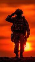 Soldier salutes against a dramatic sunset backdrop while on duty in a wartime environment photo