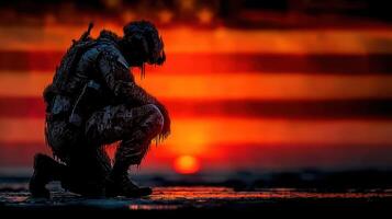 Soldier kneeling in silhouette against a vibrant sunset background featuring the American flag photo