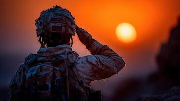 Soldier salutes the setting sun during sunset on a rocky terrain in a desert environment photo