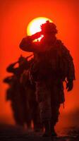 Soldiers salute as the sun sets on a military training exercise in a fiery orange sky photo