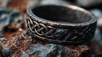 Detailed close-up of an intricately designed black ring resting on textured stones, showcasing craftsmanship and unique patterns photo