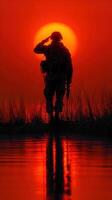 Soldier saluting against the backdrop of a vibrant sunset over a calm body of water photo