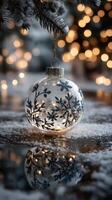 Winter holiday ornament hanging on a snow-covered branch with glimmering lights in the background photo
