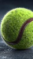 Tennis ball glistening with moisture on a dark surface after a recent match in an outdoor court setting photo