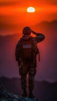 Soldier saluting the sunset while standing on a rocky peak in a mountainous region photo