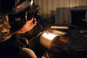 Male in face mask welds with argon welding. Industrial welder worker welding using argon machine, close up. Man working with arc welding machine in garage. photo