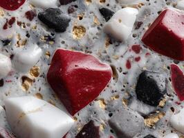 Red, white, and black stone-like shapes with gold accents set on a gray speckled surface. The arrangement is visually striking and textured, featuring varied geometric forms photo
