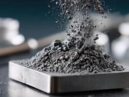 Fine black powder cascades from the air onto a square metal tray. The focus is sharp on the powder with a blurred background, highlighting texture and contrast photo