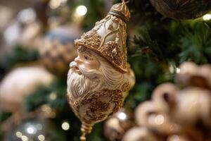 Festive holiday ornament with a Santa Claus face intricately decorated with gold accents hangs on a Christmas tree. Surrounded by blurred lights and ornaments in soft focus photo