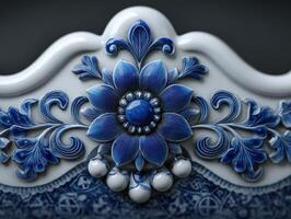 Ornate blue floral design with intricate detailing on a white ceramic surface. Central flower with layered petals and bead-like elements, surrounded by symmetrical leaf patterns photo