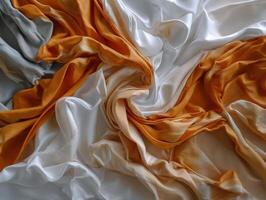 Swirling folds of smooth fabric in white, orange, and gray create an abstract pattern. The silky texture and flowing shapes evoke a sense of movement and elegance photo
