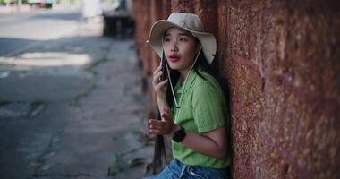 Handheld high angle view shot, Relaxed woman sits against a brick wall and chatting happily on mobile phone. video