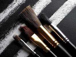 Brushes with metallic ferrules rest over black canvas featuring bold white brushstrokes. Varied bristle sizes suggest use in painting and artistic endeavors, contrasting texture visible photo