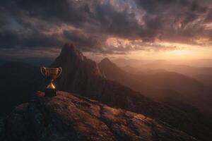 Golden trophy on rocky peak with dramatic, cloudy sky at sunset. Mountain range fades into the horizon, creating a sense of achievement and adventure. Light casts warm tones over the scene photo