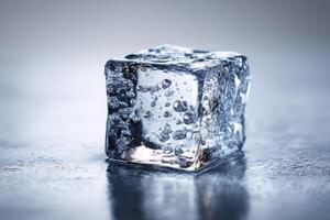 Shiny ice cube with visible air bubbles sits on a wet surface, showcasing textures and reflections. Light plays across the ice, creating a cool, refreshing ambiance in a sharp focus photo