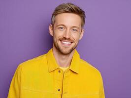 Smiling man with short light hair, wearing a bright yellow jacket and shirt, stands against a purple background. He has a well-groomed beard and appears friendly and approachable photo