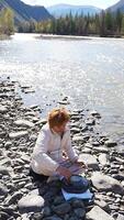Woman playing a steel tongue drum near a mountain river in Altai, surrounded by wild nature. Concept of spiritual retreat, sound healing, and ancient connection to earth. High quality 4k footage video