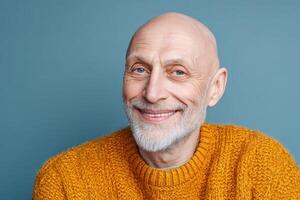 Bald man with a white beard wears a mustard yellow sweater, smiling warmly at the camera against a soft blue backdrop. The image evokes feelings of warmth and approachability photo