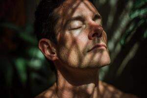 Face of a man with closed eyes, softly illuminated by sunlight filtered through leaves, creating intricate shadows on his skin, conveying a sense of calm and relaxation photo