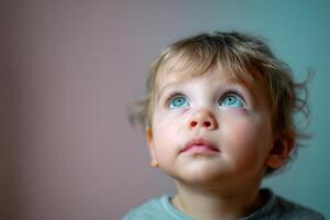 A young child with curly hair gazes upward with wide, curious eyes. Their expression is one of wonder and innocence, wearing a light-colored shirt. The background is softly blurred photo