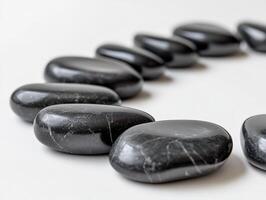 Smooth black stones with subtle white veins are arranged in a semi-circle formation, focusing on the front stones, while the background stones gradually blur, creating a sense of depth photo