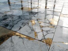 Marble tiles with gray and white tones, featuring reflective gold veins, create a luxurious pattern. Light reflects on the polished surface, accentuating the intricate design photo