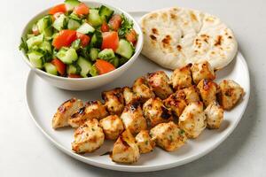 Appetizing chicken kabobs are served with a fresh salad and delicious flatbread on a plate photo