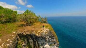 FPV drone shot of woman practicing yoga on dramatic cliff above turquoise ocean on Nusa Penida, Bali, Indonesia. Concept of freedom, mindfulness, and nature connection. video