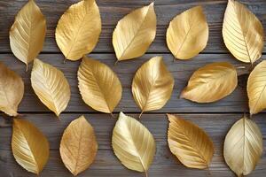 Glistening golden leaves are neatly arranged on a textured, rustic wood surface to form patterns photo