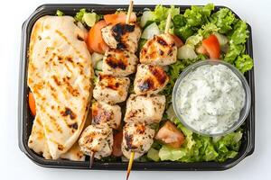 Grilled chicken skewers with pita bread, greens, tomatoes, cucumbers, and tzatziki sauce fill container photo