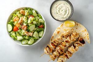 Grilled chicken skewers with salad and tzatziki sauce present a delicious Mediterranean culinary experience photo