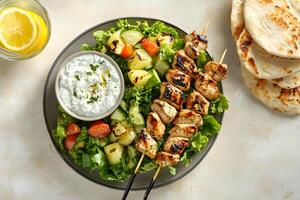 Grilled chicken skewers, tzatziki, cucumber salad, and pita bread make a delicious meal photo