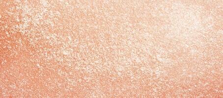 Peach colored grainy surface is covered with white specks creating a textured pattern photo