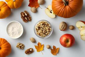 Pumpkins, apples, and fall leaves are arranged with walnuts and flour on a white backdrop photo