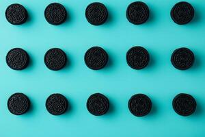Rows of textured black cookies are neatly organized on a vibrant light blue backdrop photo