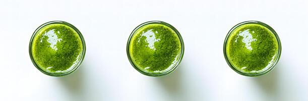 Three glasses of vibrant green smoothie are arranged elegantly on a bright white surface photo