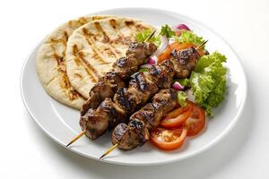 Three meat skewers sit with flatbread and salad on a bright white plate photo