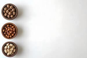 Three wooden bowls hold walnuts, hazelnuts, and pistachios, positioned vertically on a white background photo