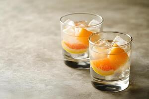 Two clear glasses showcase sparkling beverages with ice and orange slices on stone surface photo