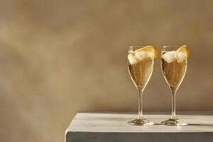 Two wine glasses hold sparkling champagne with ice and lemon on beige surface photo