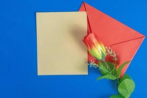 Red envelope with a blank card and a rose on a blue background. photo